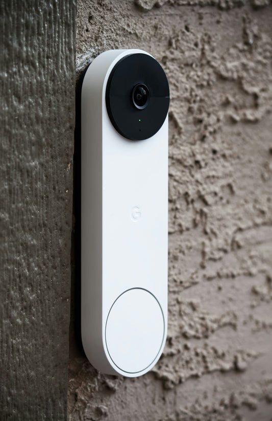 A photo of a White Google Nest Door Bell which is has a black Camera at the top and a White Button at the bottom